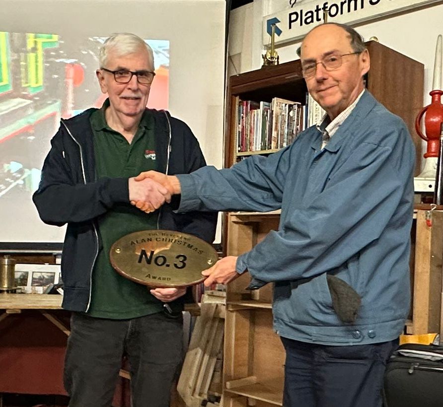 Standing in the SWRS Manor meeting place, surrounded by railwayana, Frank Taylor presents the replica brass oval cab numberplate that is the Society's Reverend Alan Christmas Award, to Richard Fillmore.